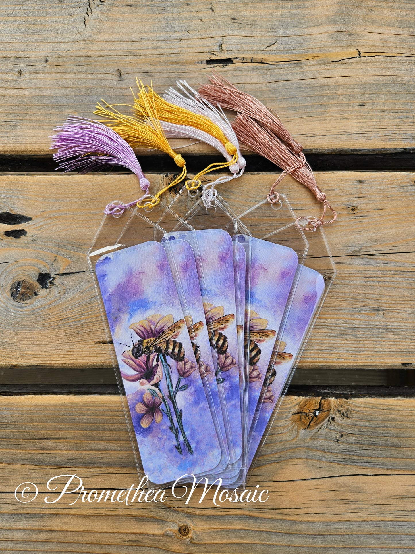 flat lay of pastel purple and pink bee with flower bookmarks in reusable clear sleeves and assorted tassels