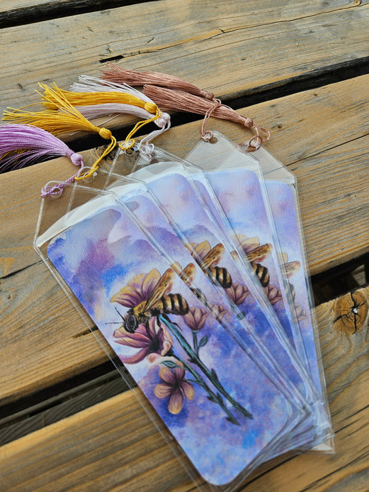 Honeybee bookmarks in protective clear sleeves with assorted colored tassels on wooden table