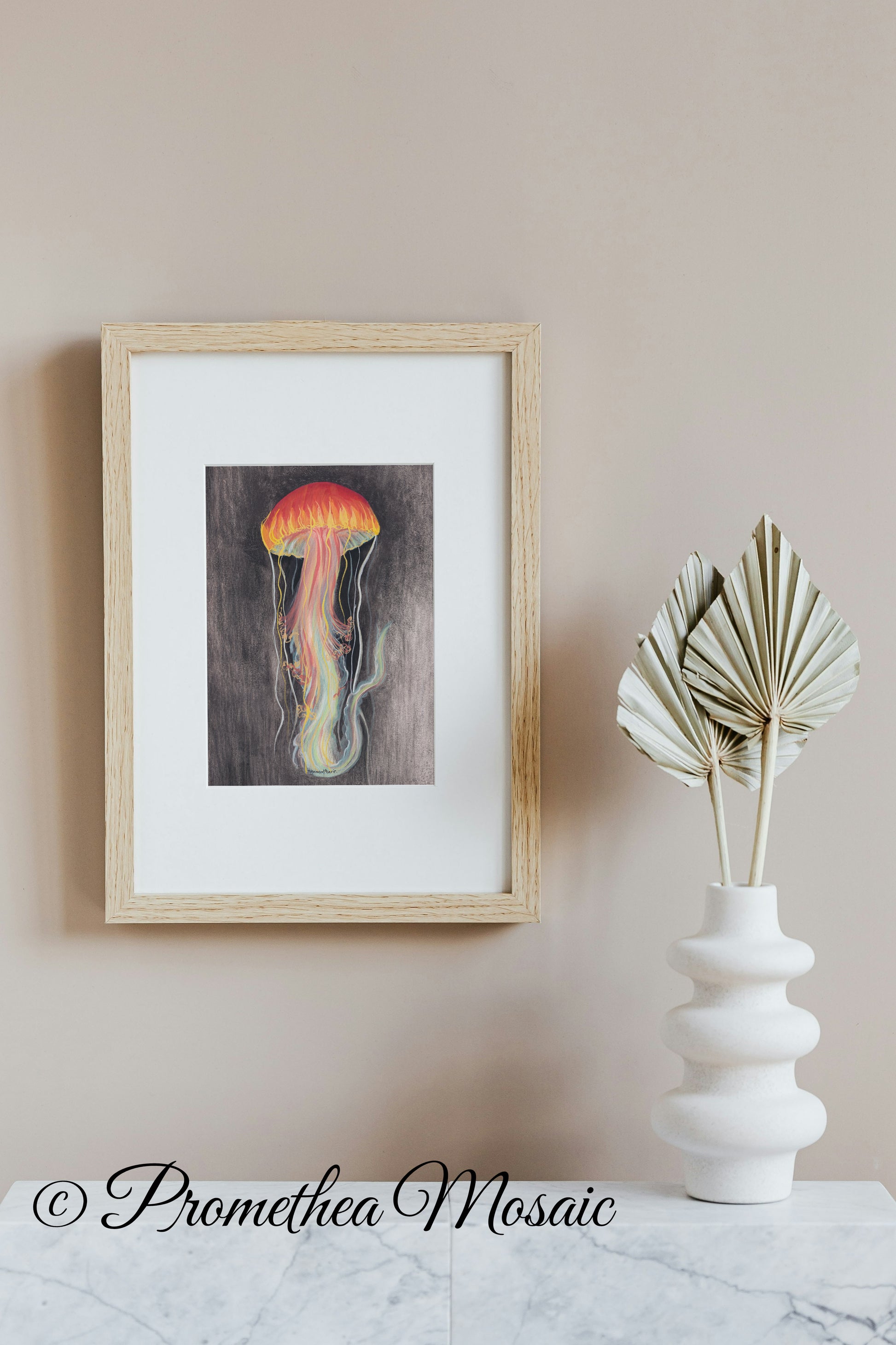 Framed art print of a jellyfish on a wall next to a white vase with dried leaves.