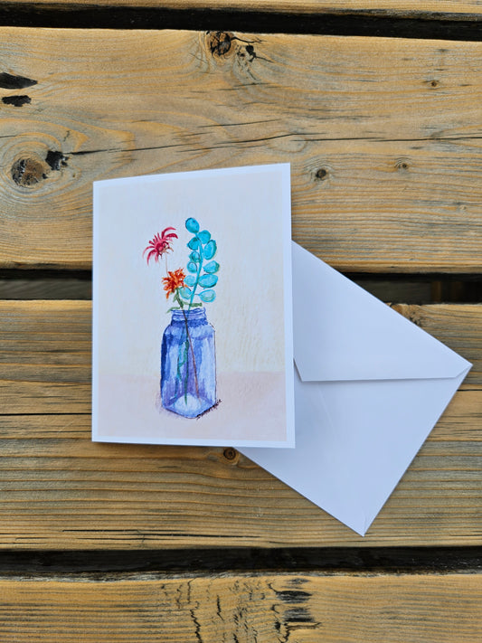 botanical wildflower greeting card featuring flowers in blue vase against a yellow and peach background. Displayed with white envelope.