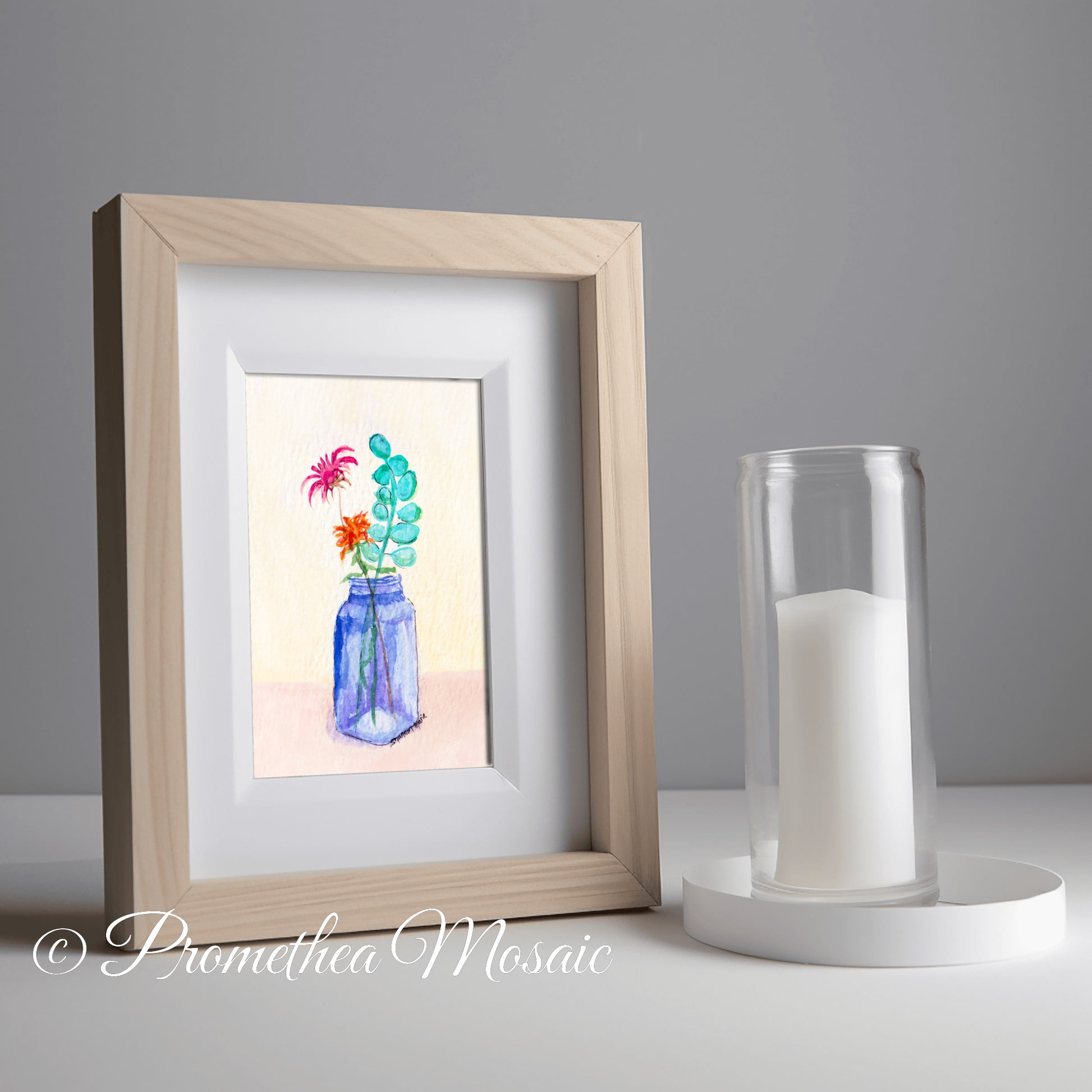 Framed artwork of flowers in a blue bottle next to a candle holder in kitchen on a gray background