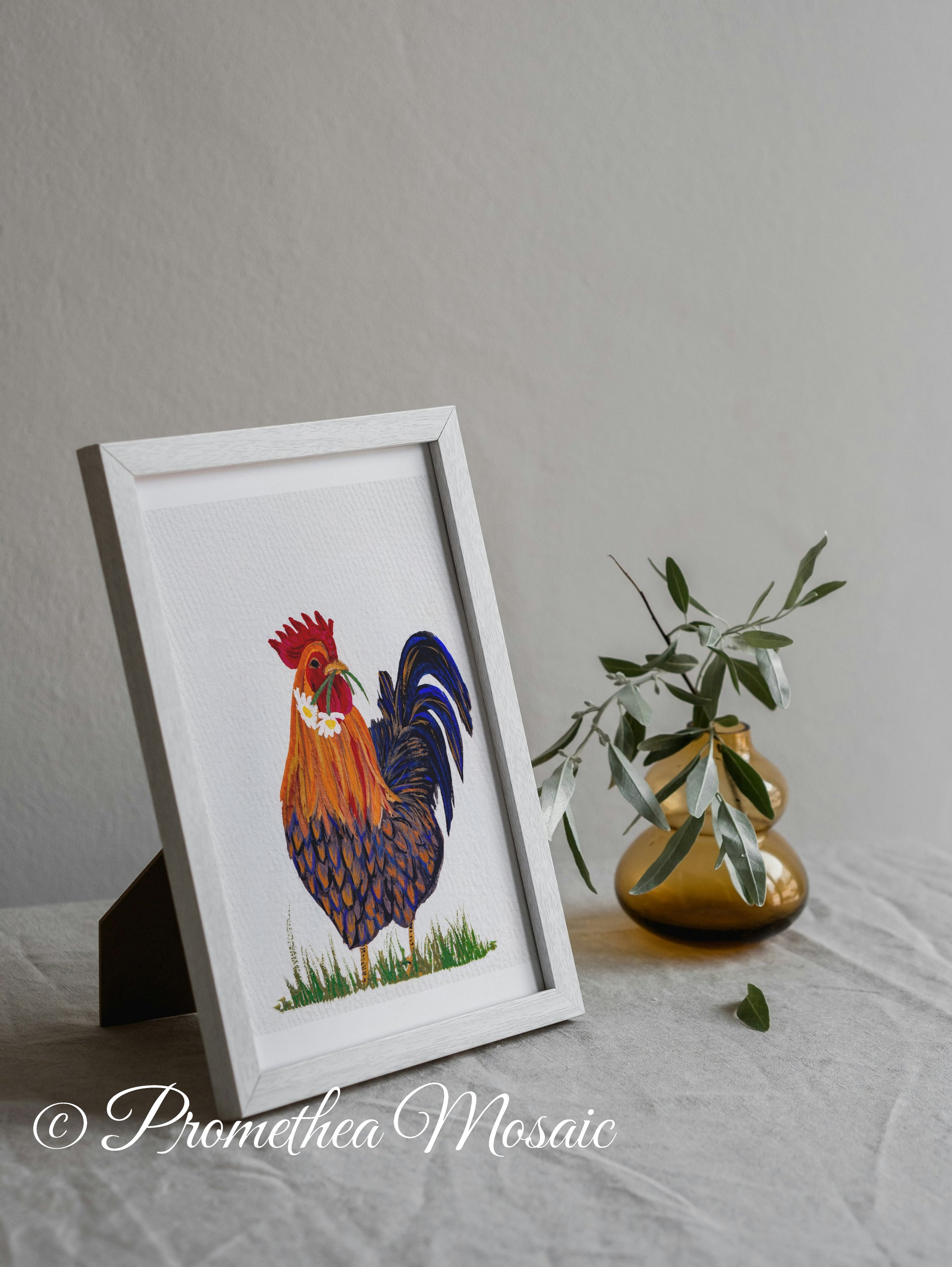 Framed artwork of a rooster on a gray surface with a vase and eucalyptus plant in the background.