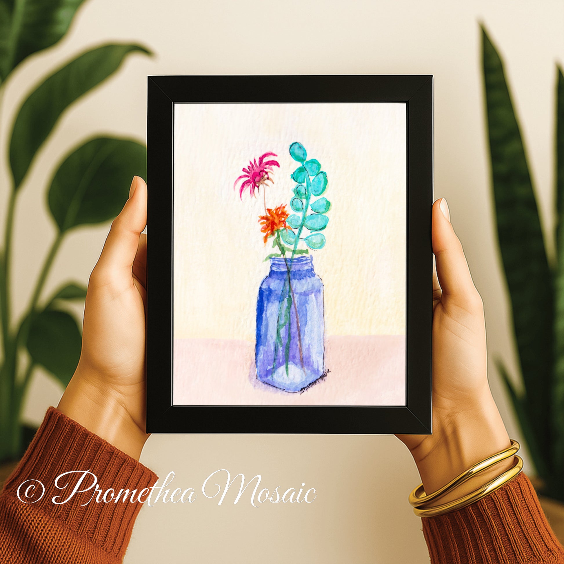 Framed artwork of flowers in a blue jar held by a person with plants in the background
